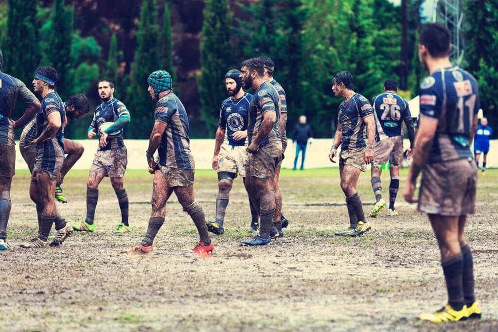 A male rugby team covered in dirt, playing rugby on a muddy field.
