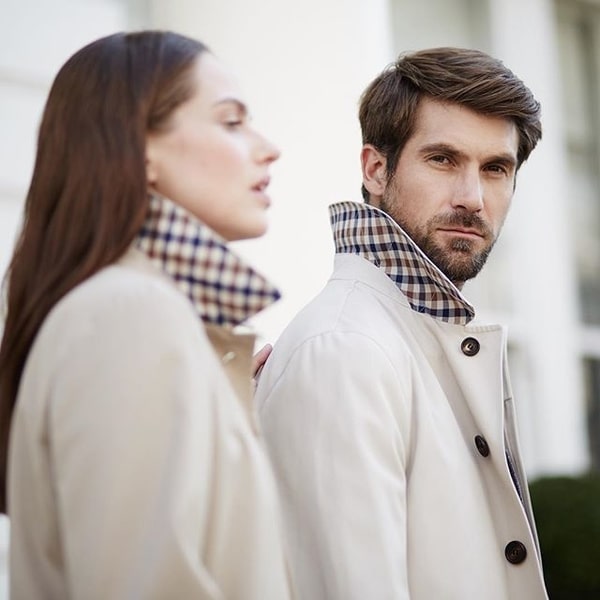 man and women in matching cream coats, man is looking at camera.