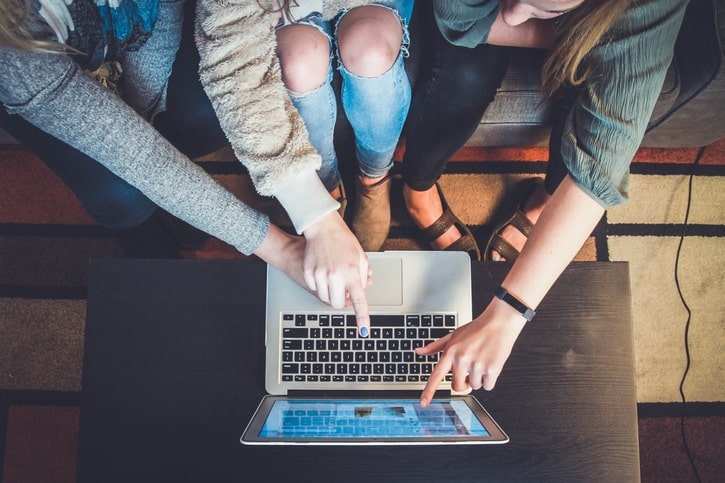 Three people sat down pointing at the screen of a laptop