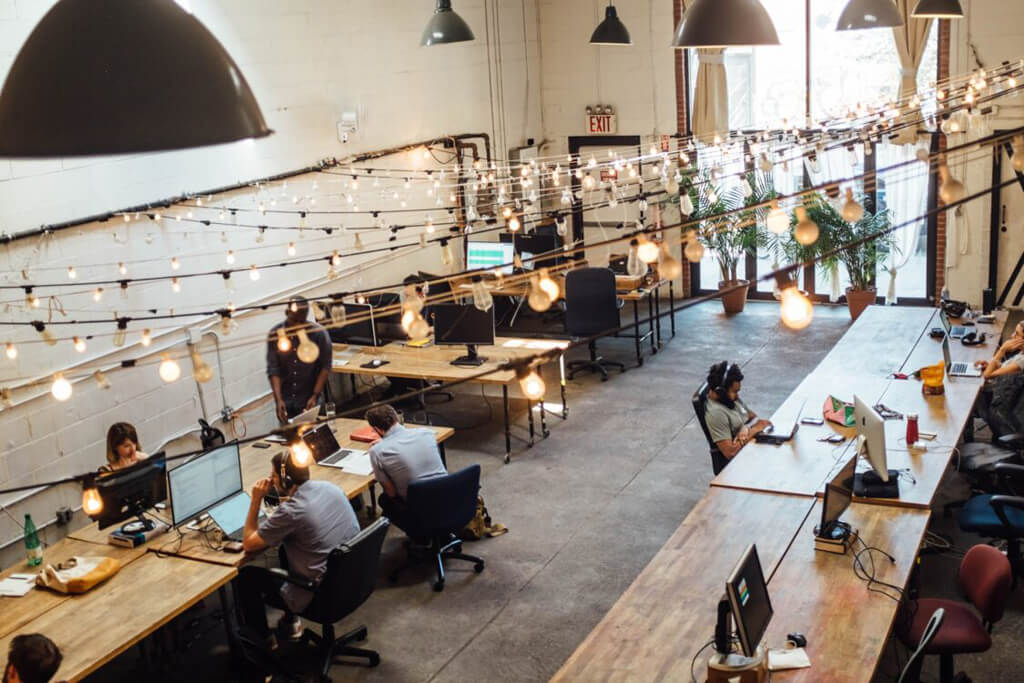 Business professionals working at large wood desks within a large open office space with large hanging lights