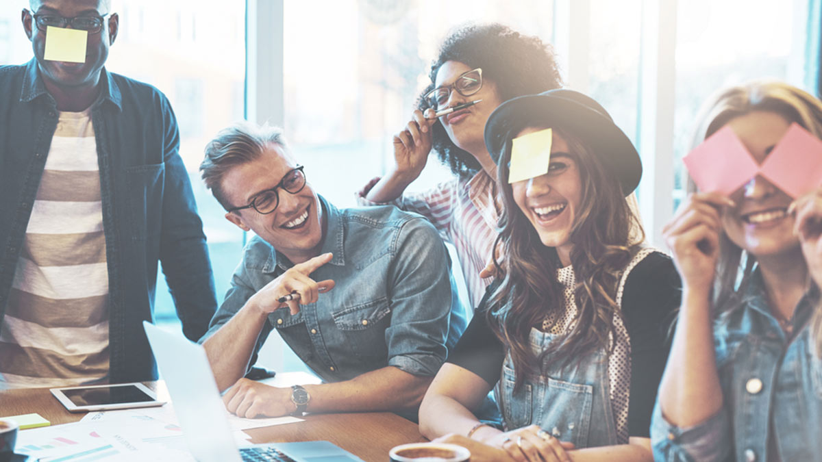 Photograph of a group of young colleagues doing team building at work with sticky notes on their heads