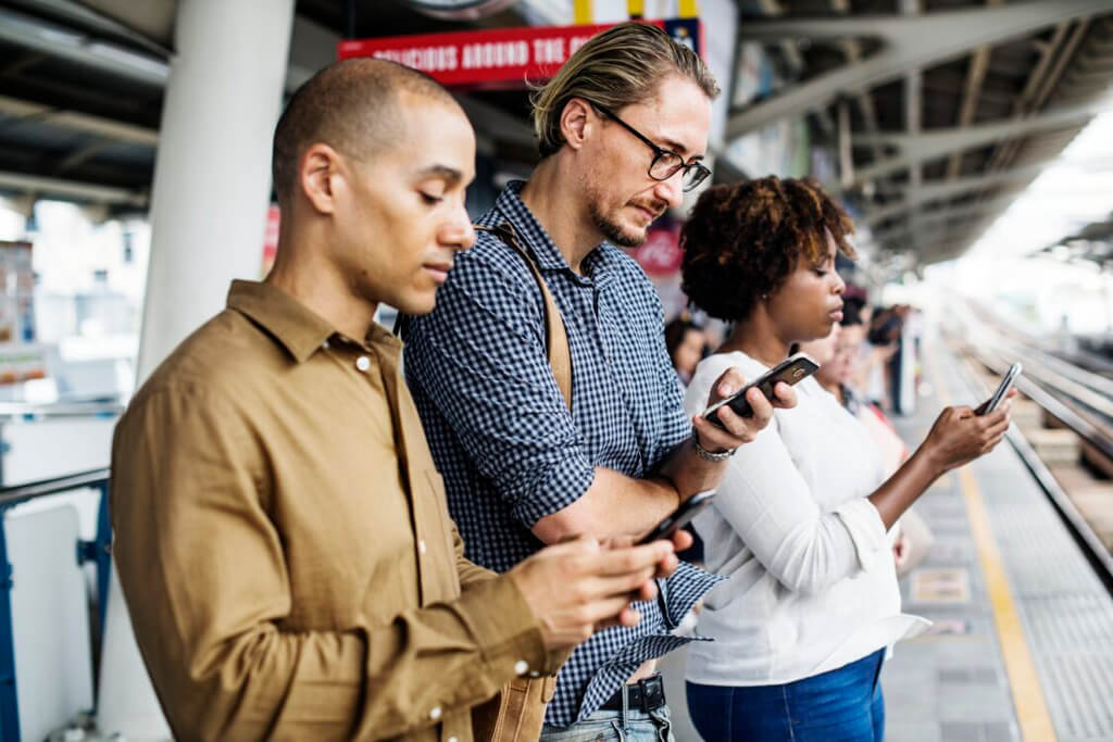 Commuters waiting in a station for a train, and using their mobile devices.